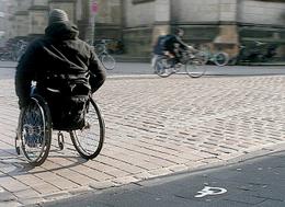 Bild zeigt einen Rollstuhlfahrer bei einer barrierefreien Überquerung einer Straße mit Kopfsteinpflaster (vergrößerte Bildansicht wird geöffnet)